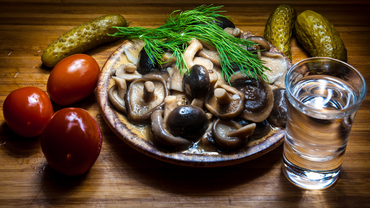 Рюмка водки на столе с солеными грибами, помидорами и огурцами