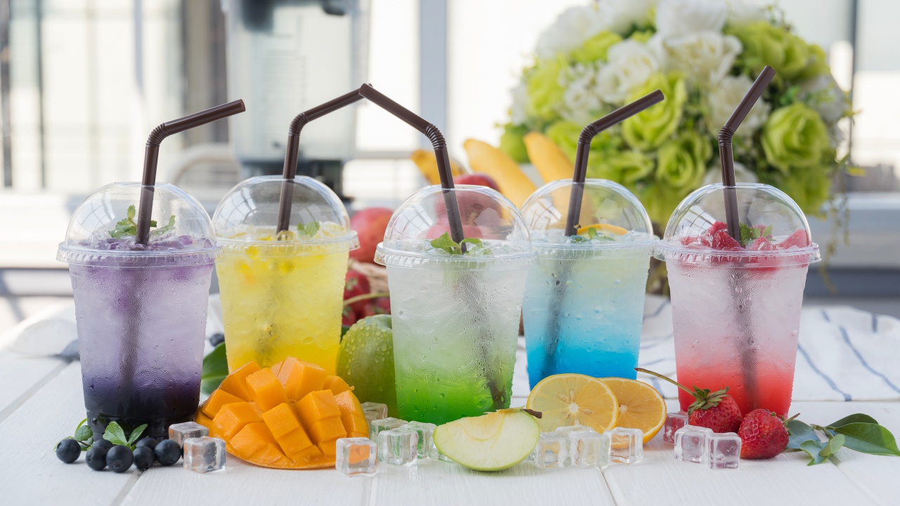 Коктейли в стаканах с трубочками на столе с кубиками льда и фруктами