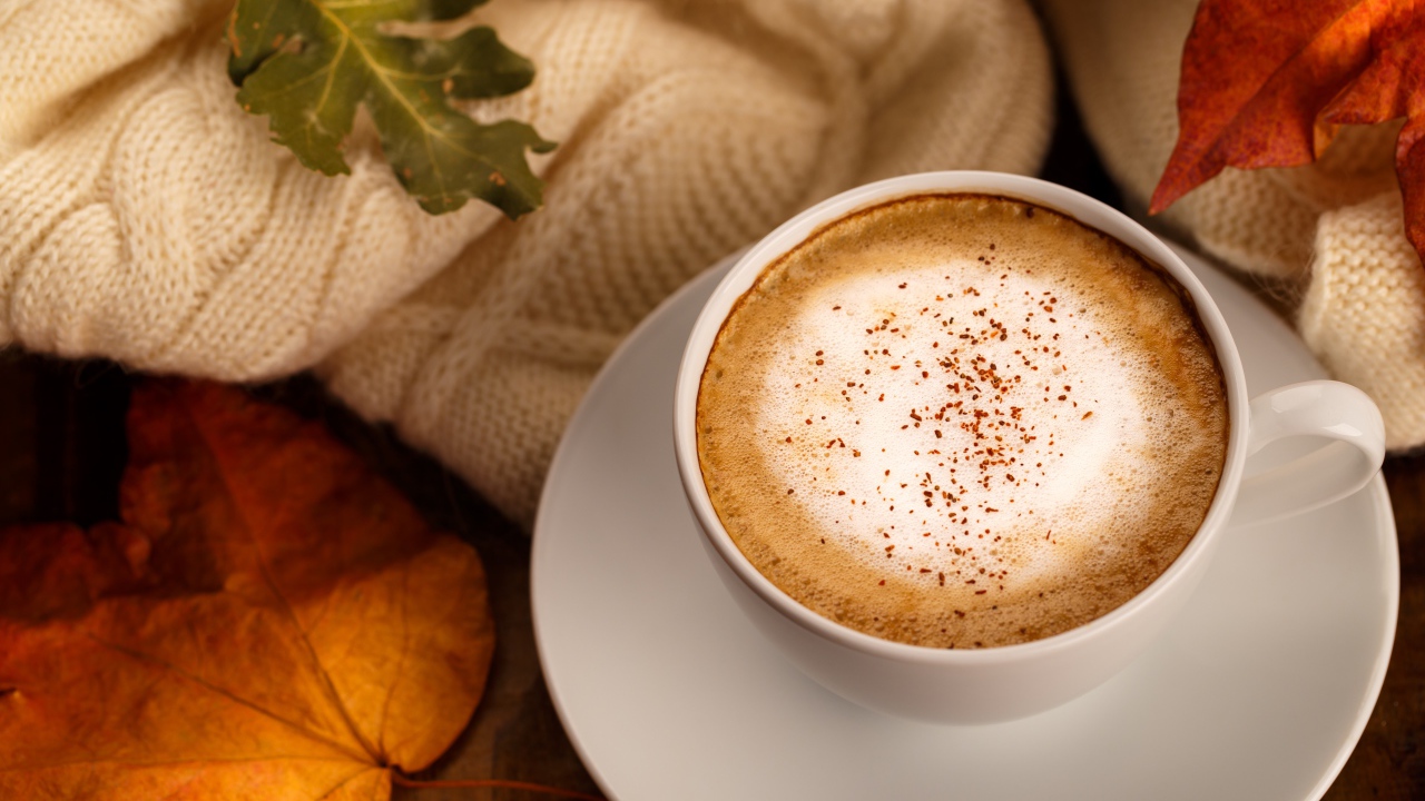 Белая чашка с вкусным кофе на столе с желтыми листьями