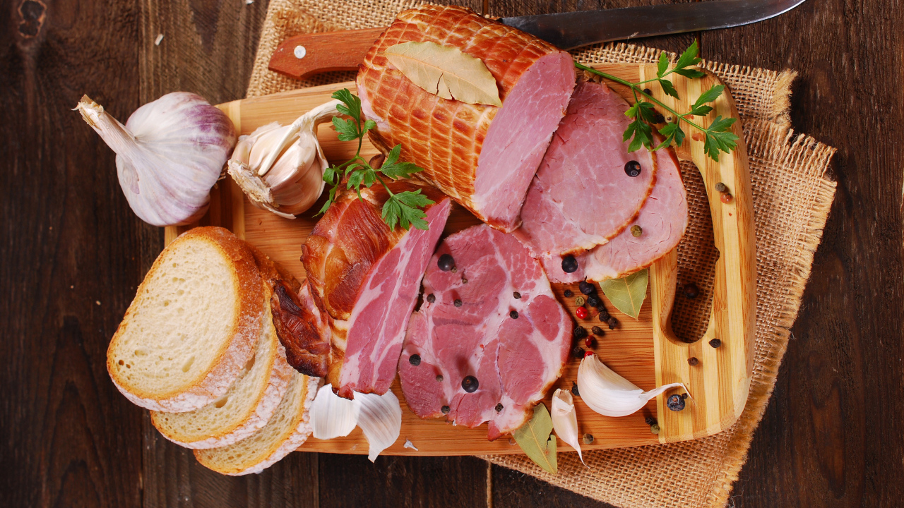 Аппетитная ветчина, чеснок и кусочки хлеба на разделочной доске