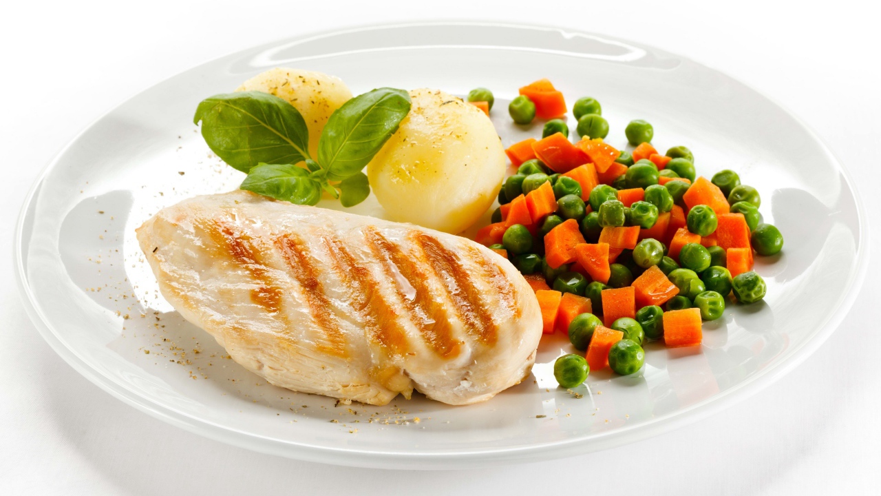 Куриная грудка на белой тарелке с картофелем, морковью и зеленым горошком