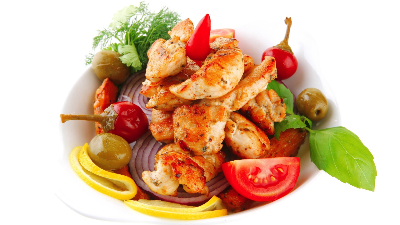 Жареные кусочки курицы на тарелке с овощами и зеленью 