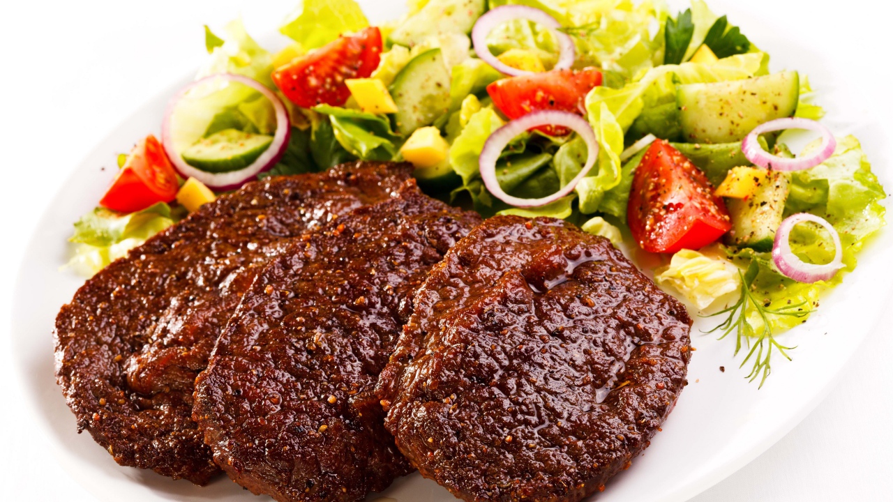 Три котлеты на тарелке с салатом на белом фоне