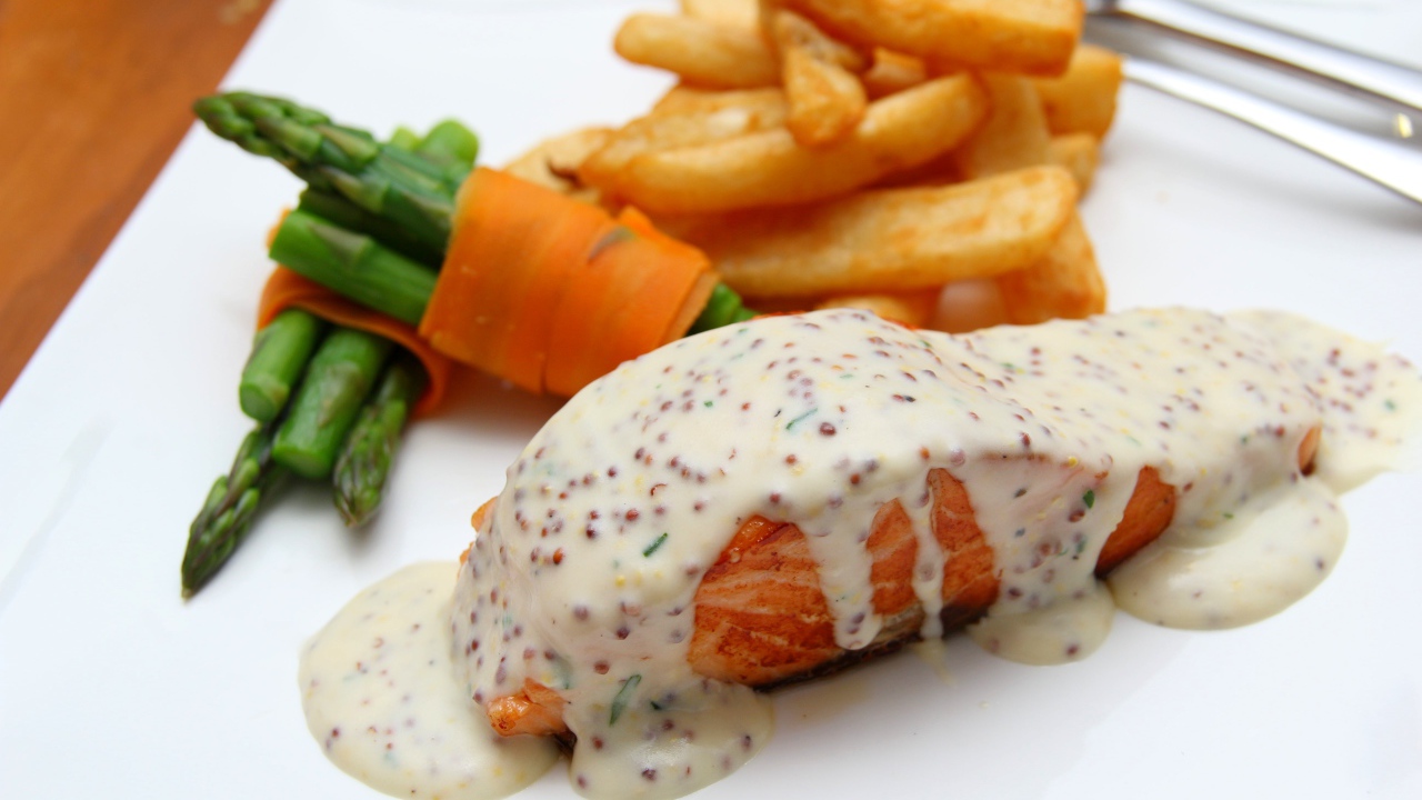 Кусок жареной красной рыбы с соусом на тарелке с картофелем фри 