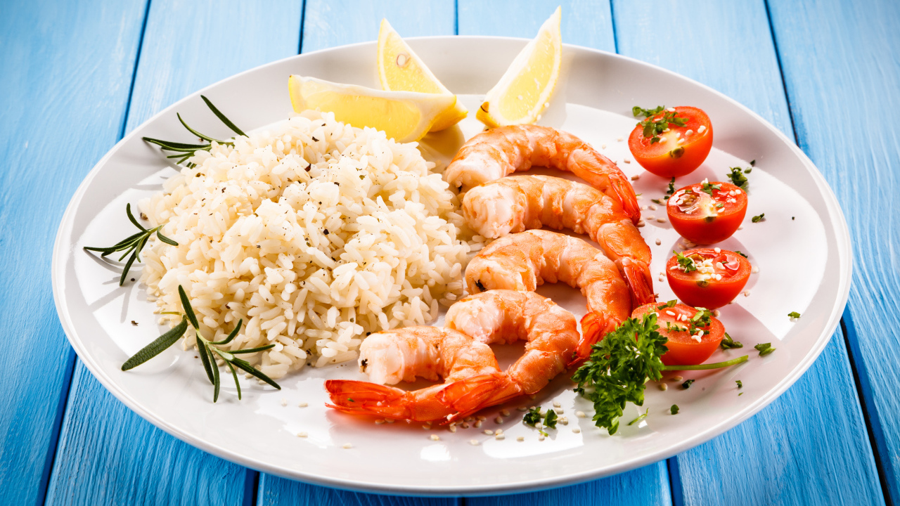 Креветки на тарелке с рисом, помидорами и лимоном