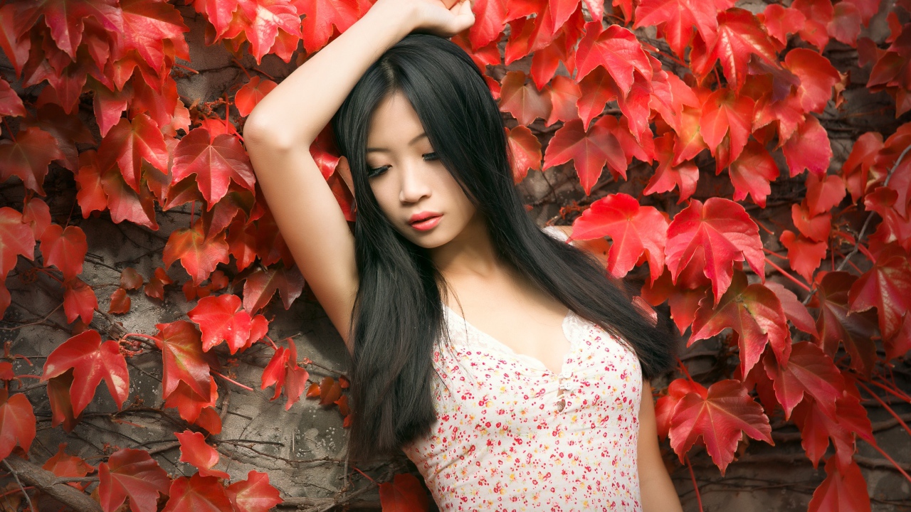 Молодая девушка азиатка стоит у стены с красными листьями