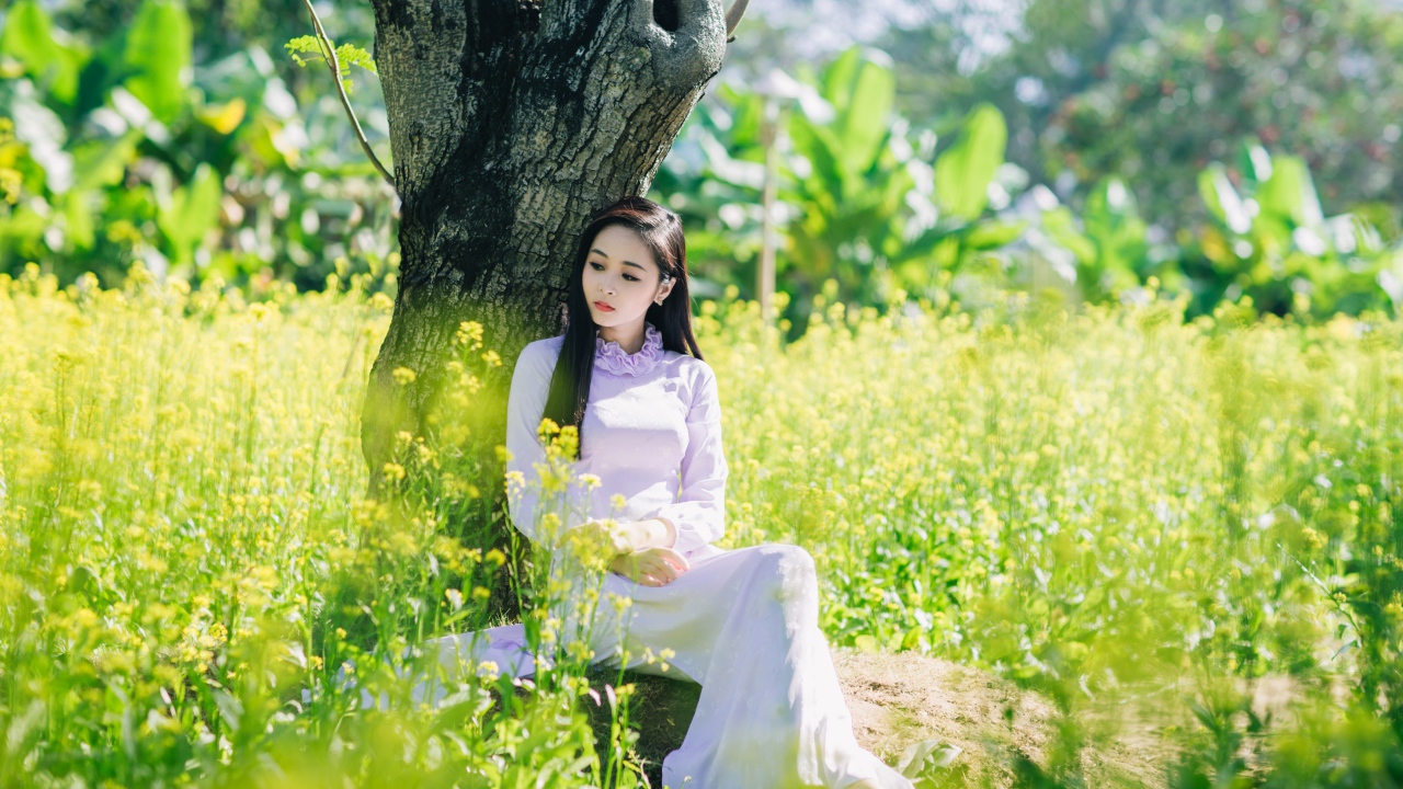 Красивая девушка азиатка сидит в белом платье под деревом