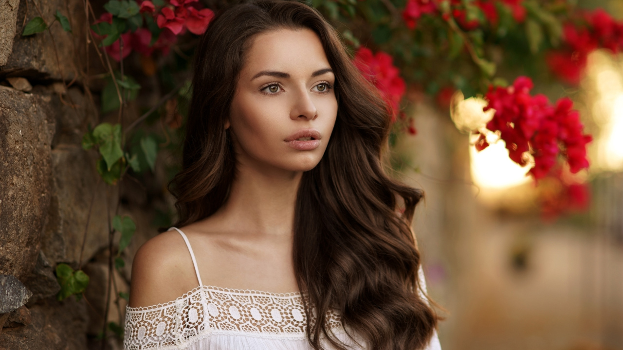 Красивая шатенка у стены на фоне красных цветов