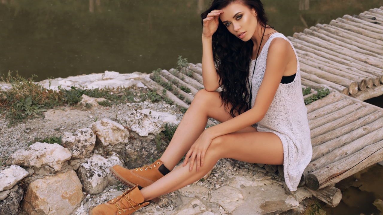 Красивая девушка брюнетка сидит у воды на мостике