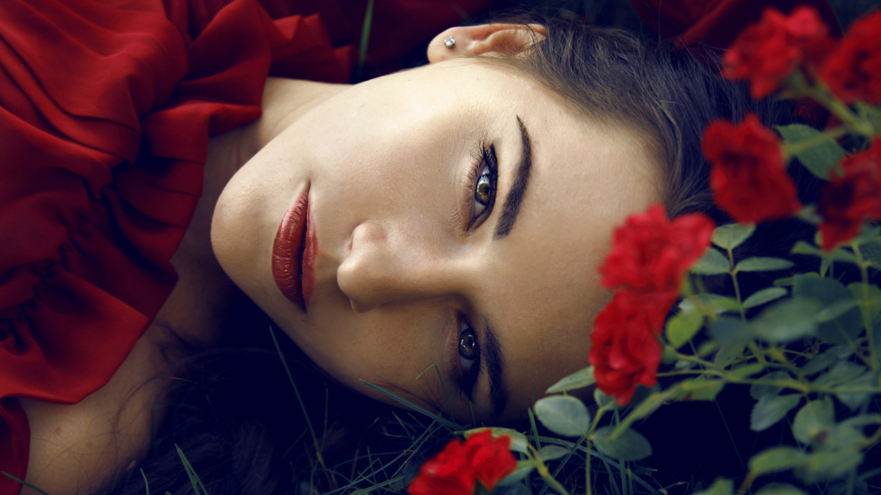 Красивая брюнетка лежит на траве с красными розами