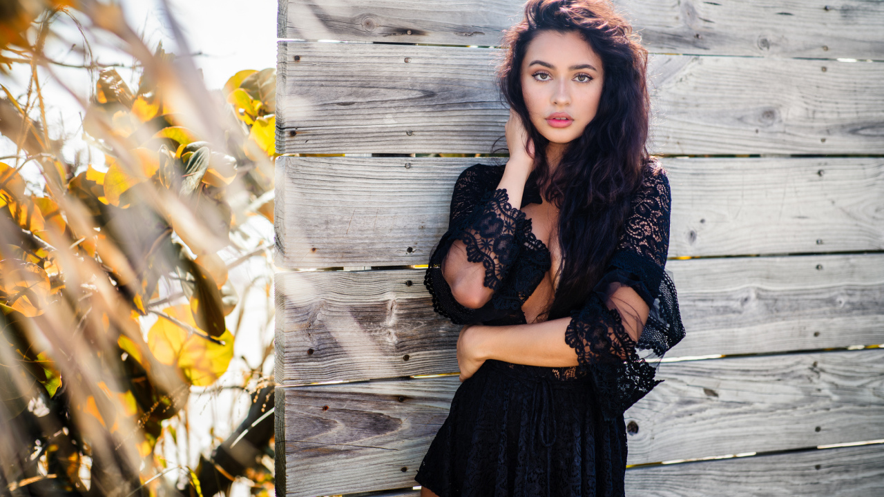 Красивая девушка в черном платье у стены 