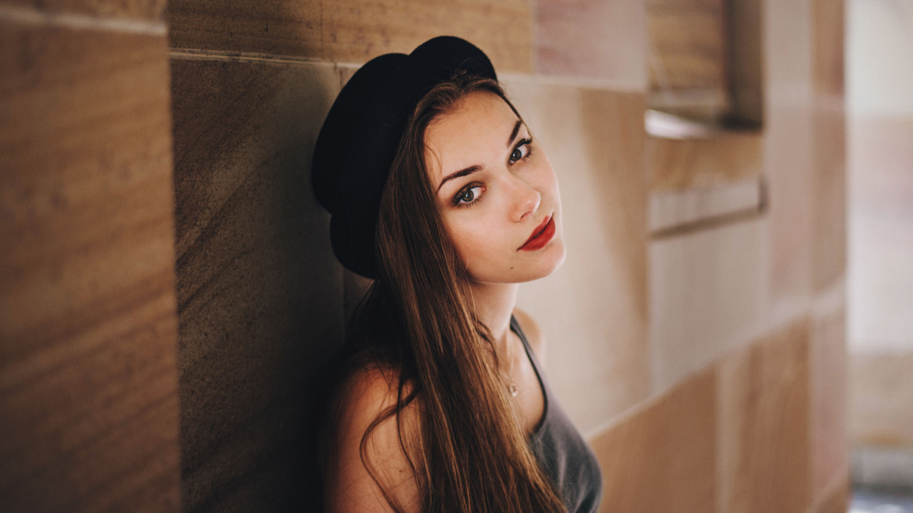 Красивая девушка в черной шляпе у стены 