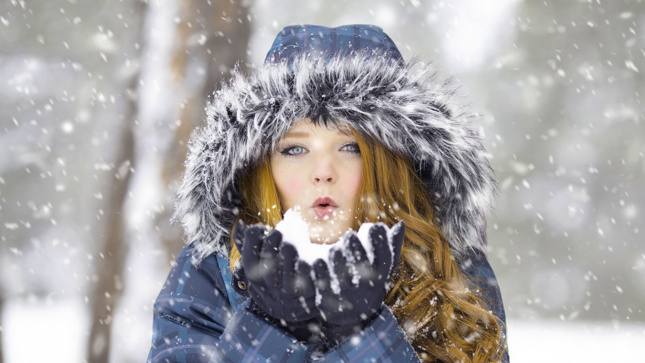 Красивая девушка в теплой куртке со снегом в руках