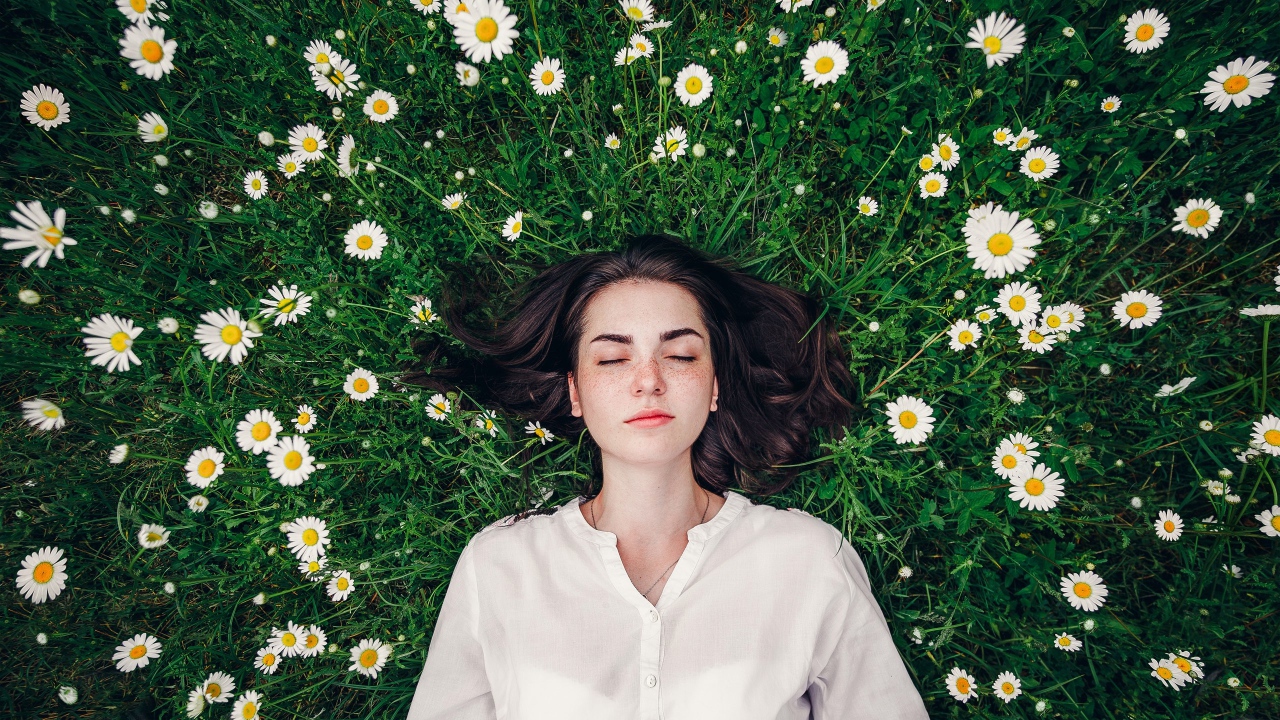 Красивая девушка лежит на зеленой траве с ромашками