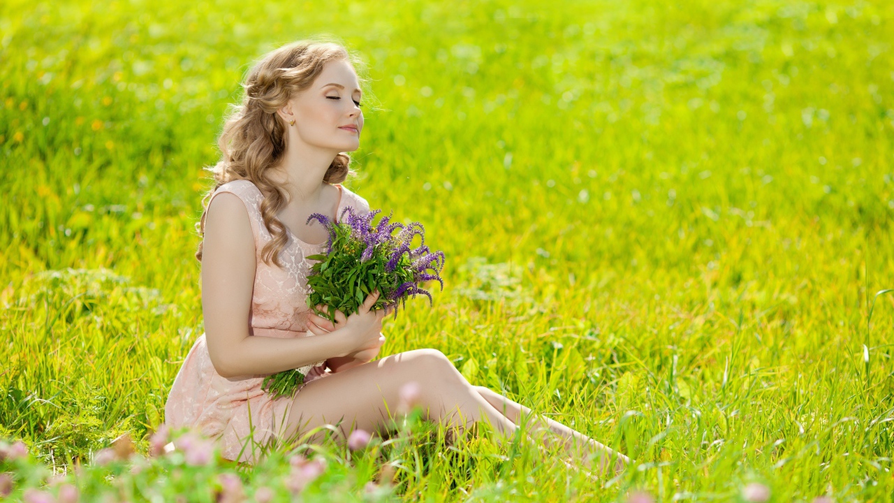 Красивая девушка с букетом сидит на зеленой траве
