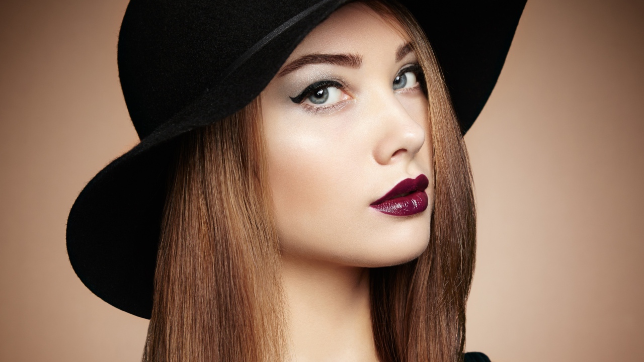 Красивая девушка с ярким макияжем в большой черной шляпе