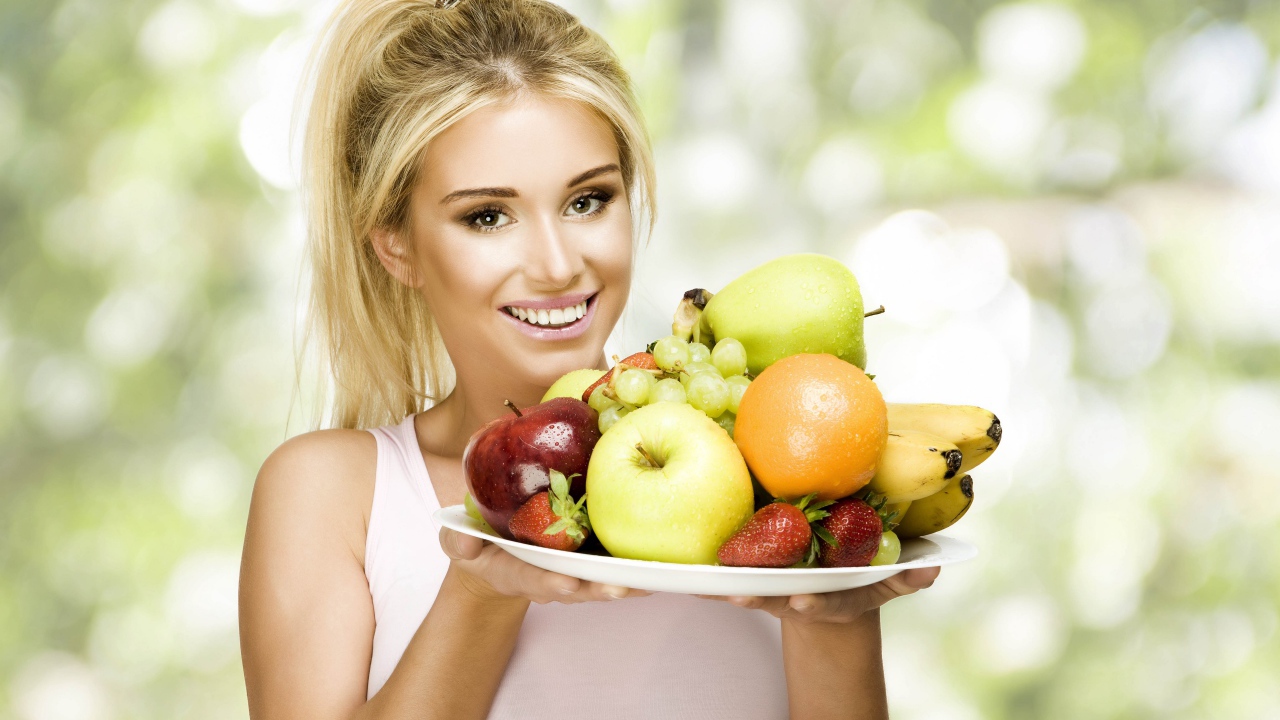 Красивая улыбающаяся блондинка с тарелкой с фруктами в руках