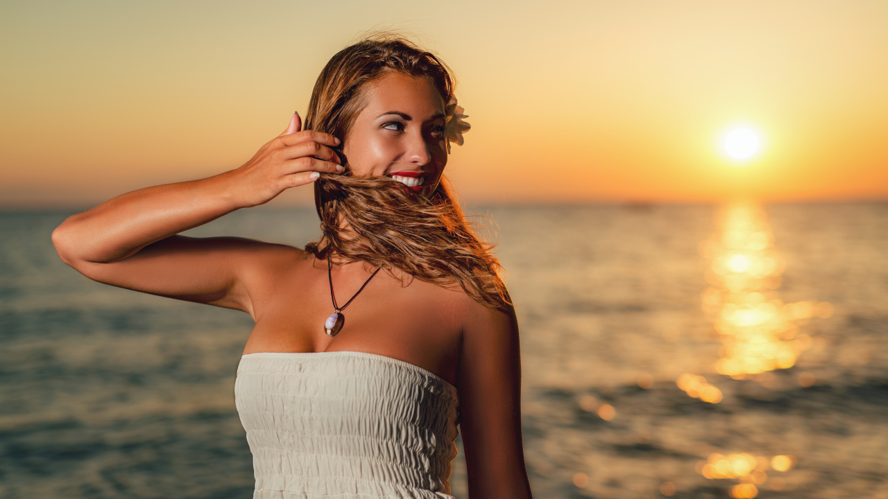 Очаровательная улыбающаяся девушка шатенка на берегу моря на закате