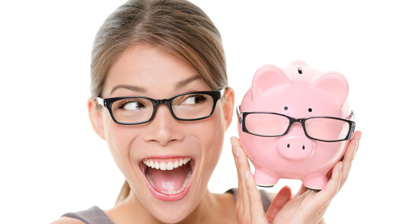 Веселая девушка в очках с копилкой в руках на белом фоне