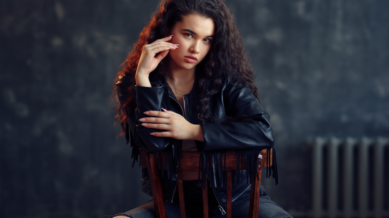 Модная красивая девушка в черное кожаной куртке сидит на стуле