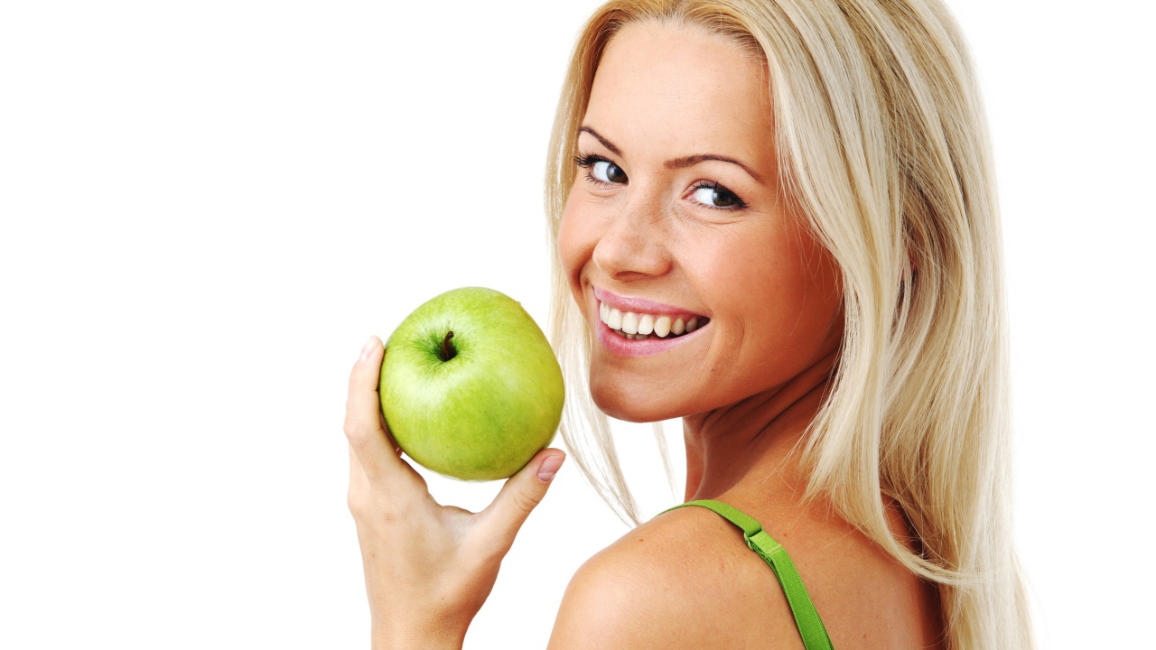 Улыбающаяся девушка блондинка с зеленым яблоком в руке на белом фоне