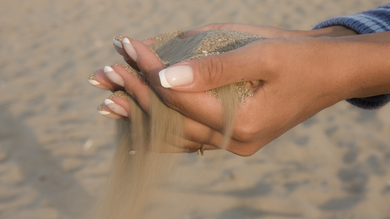 Желтый песок в руках у девушки с красивым маникюром