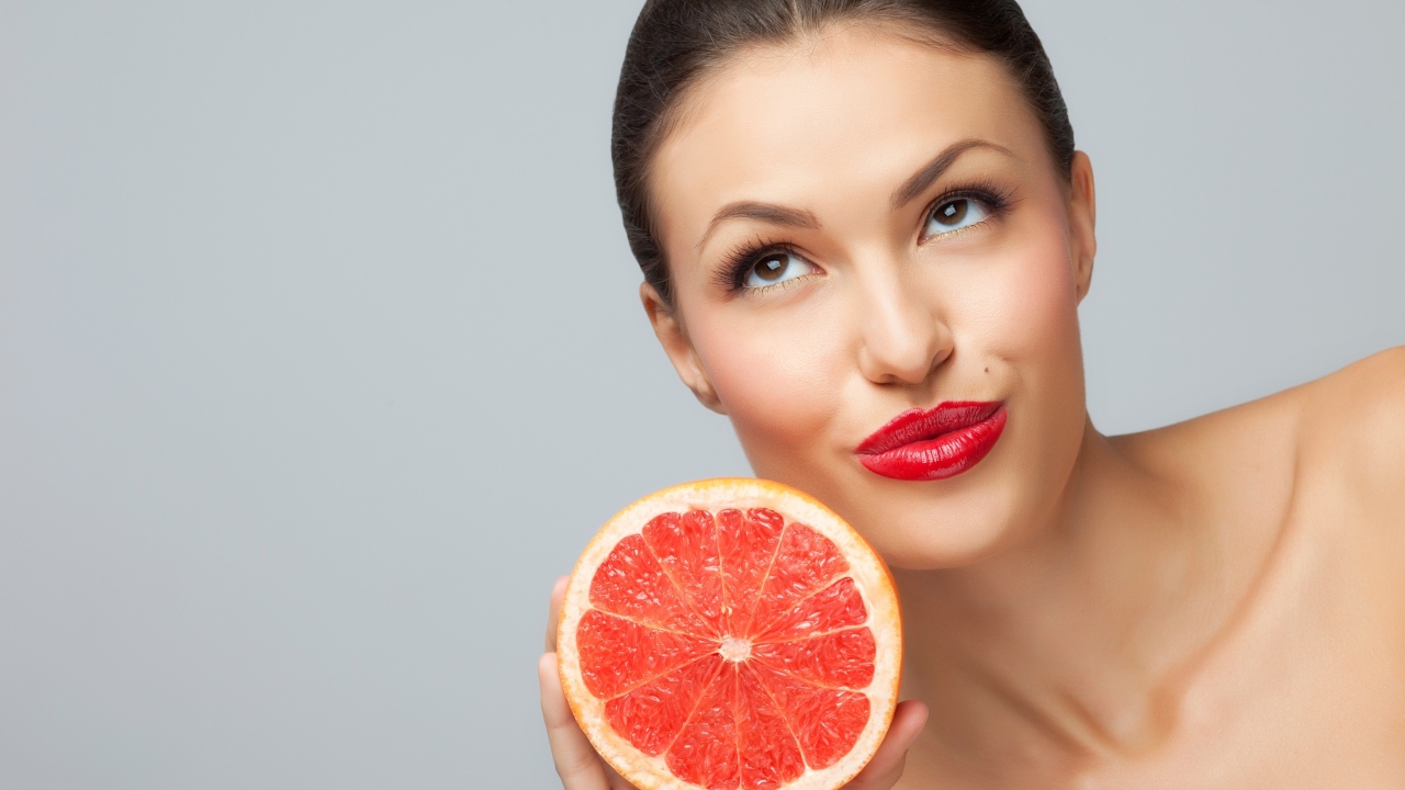 Молодая девушка с красными губами с половиной грейпфрута
