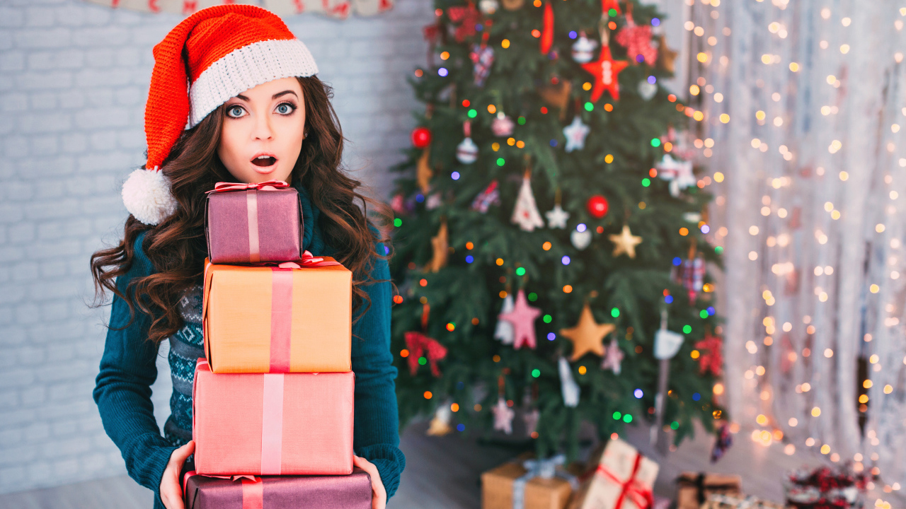 Удивленная девушка с подарками у новогодней елки 