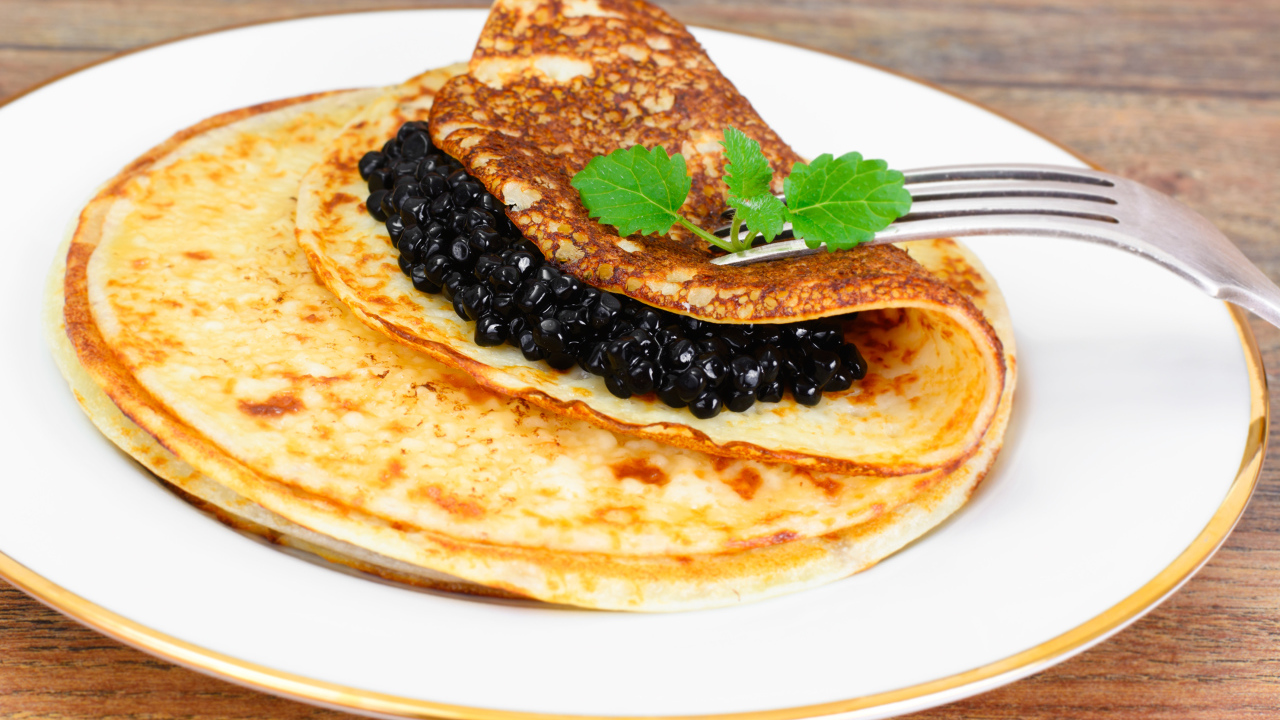 Блины с черной икрой на тарелке с вилкой