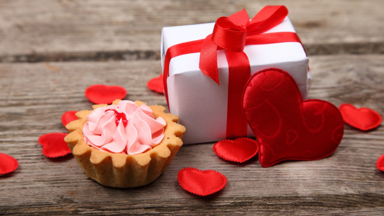 Пирожное, подарок и сердечки на деревянном фоне на День Святого Валентина