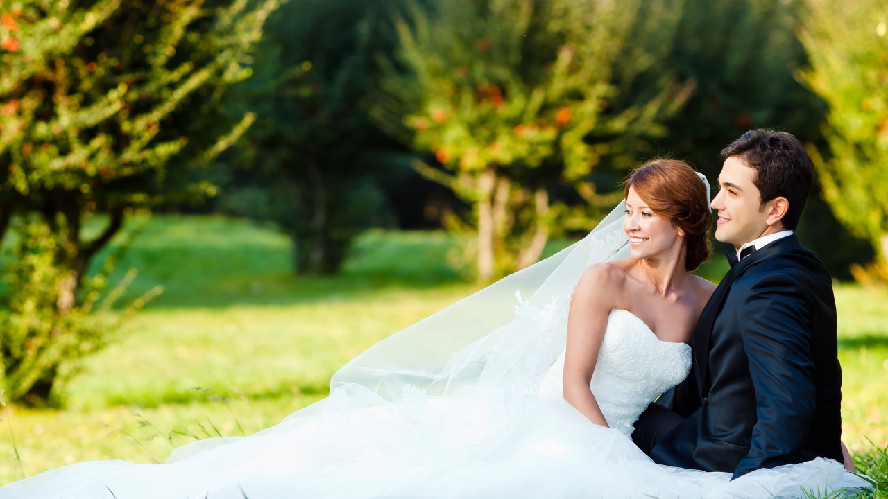 Счастливые жених и невеста сидят на зеленой траве