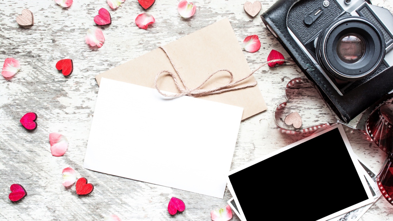 Старый фотоаппарат с фотографиями и маленькими сердечками на столе
