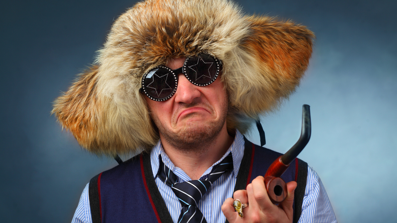 Мужчина в меховой шапке в модных очках с трубкой в руке