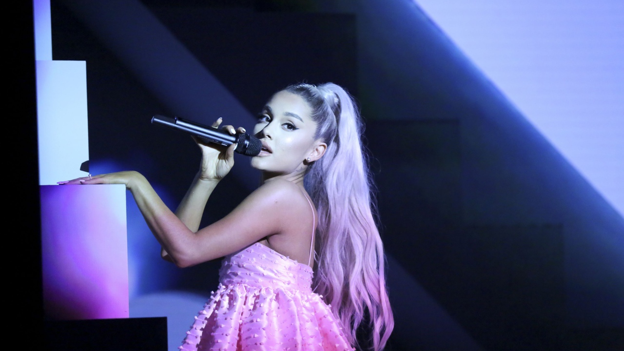 Певица Ариана Гранде на сцене с микрофоном в розовом платье