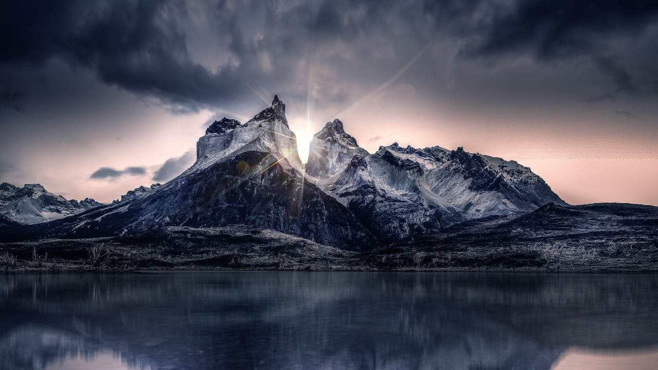 Рассвет солнца над горами у озера под пасмурным небом