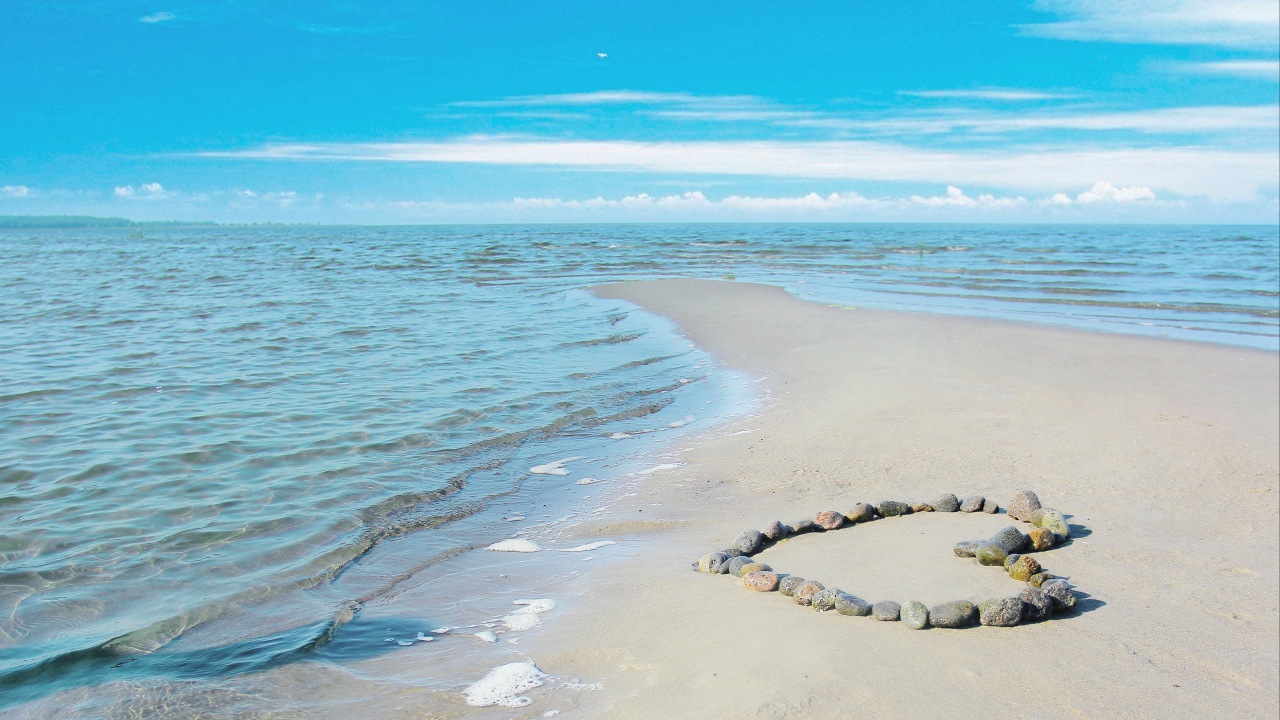 Сердце из камней на песке у спокойного моря под голубым небом