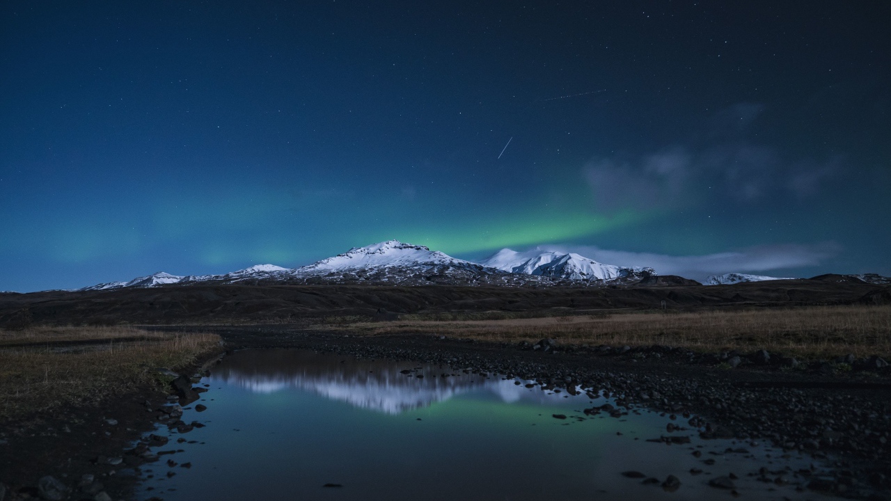 Горы и небо отражаются в луже на дороге ночью 