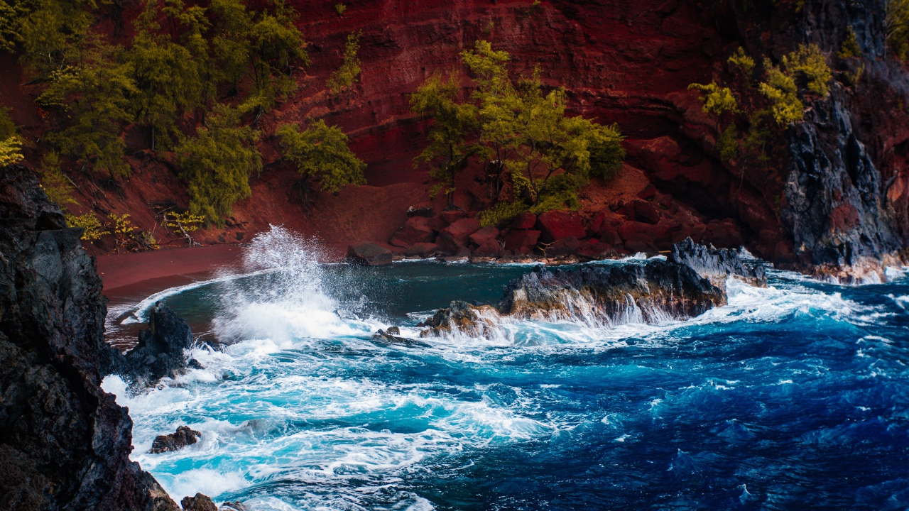 Грубое море брызгает камнями перед красным песчаным океанским заливом в Хане