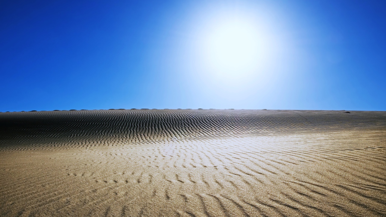 Волнистый песок в пустыне под палящим солнцем в голубом небе 