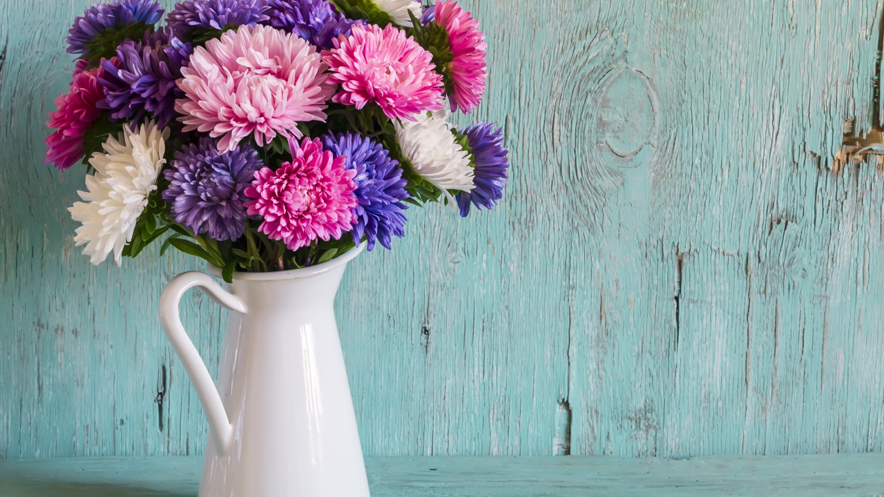 Разноцветные астры в вазе на деревянном фоне