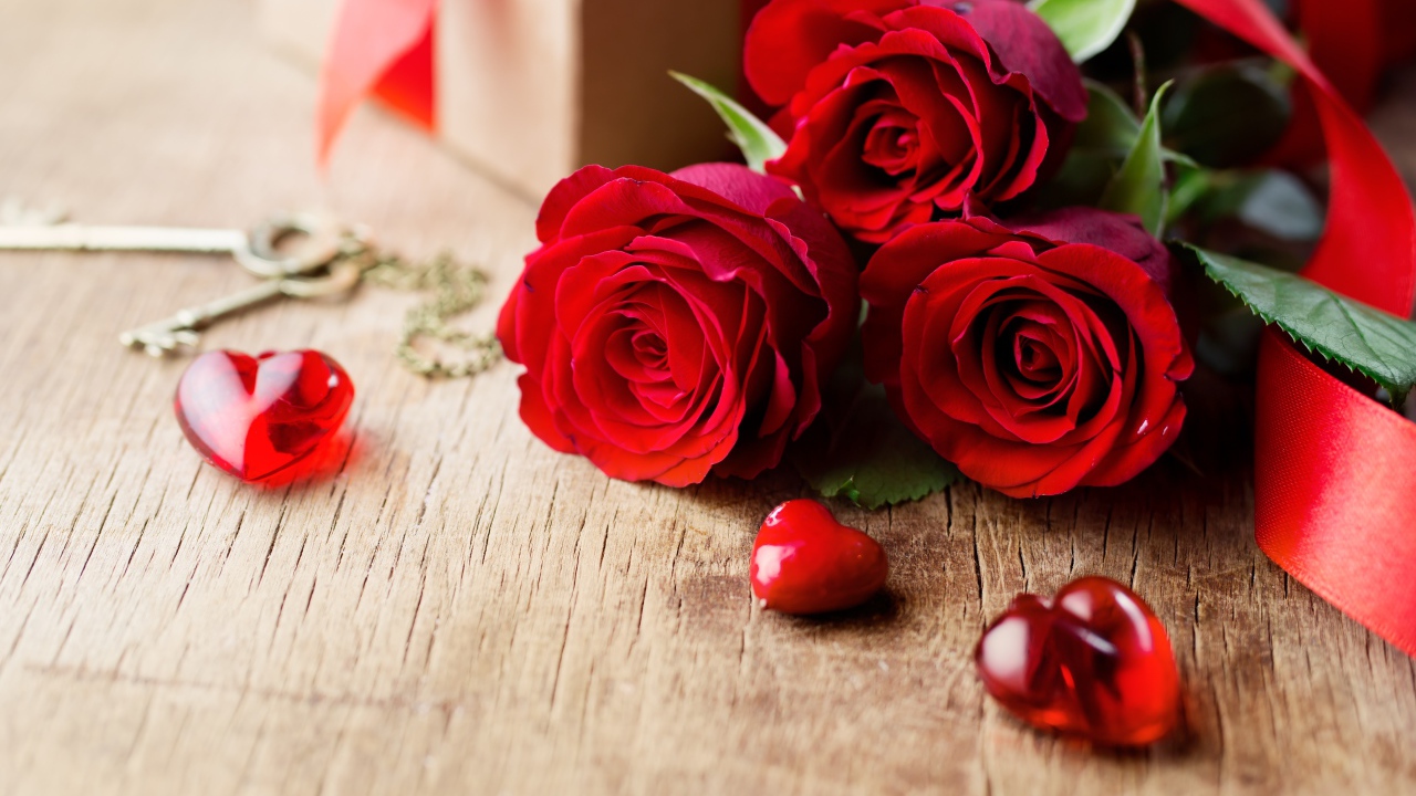 Три красных розы на деревянном столе с красными сердечками