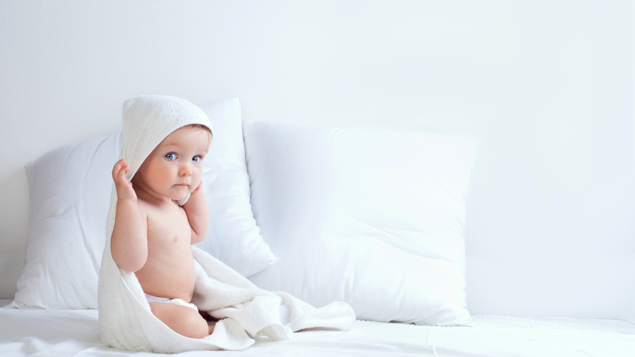 Грудной ребенок сидит на кровати с подушками