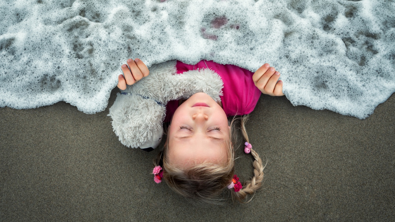 Маленькая девочка спит на песке под одеялом из морской пены