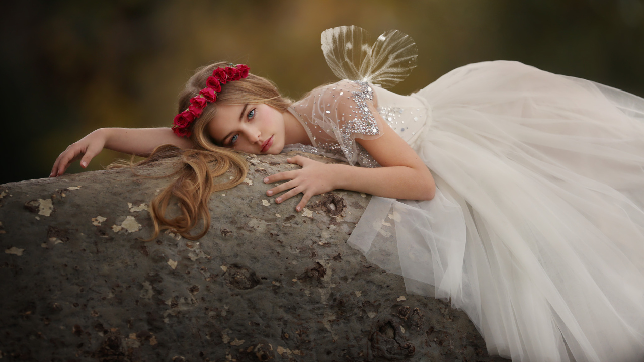 Красивая маленькая девочка в белом платье лежит на камне