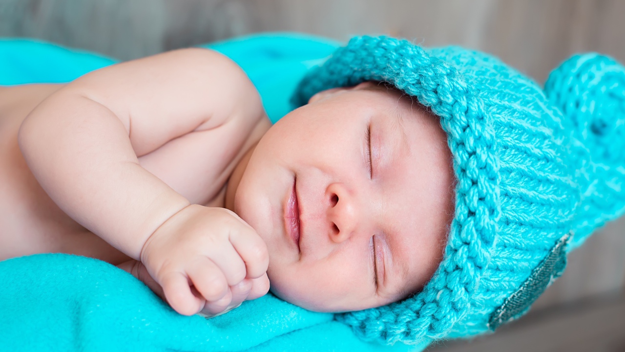 Милый спящий ребенок в голубой вязаной шапке