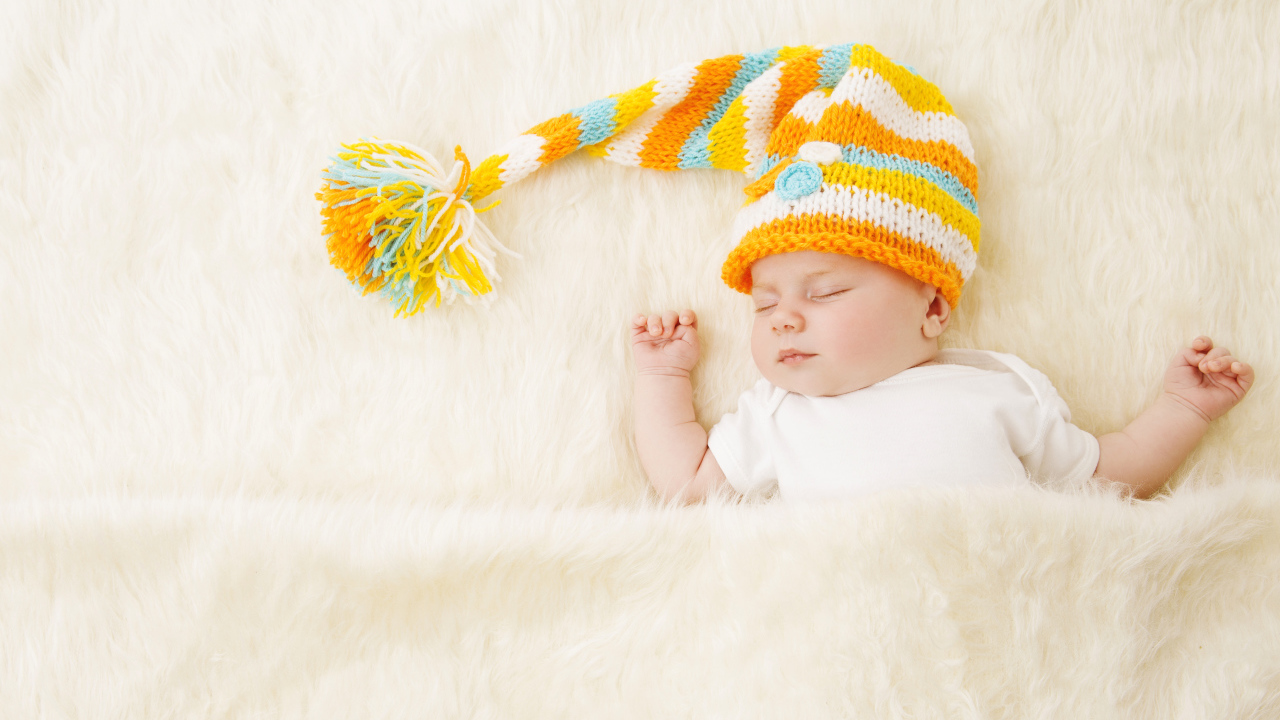 Маленький спящий под меховым покрывалом малыш в вязаной шапке