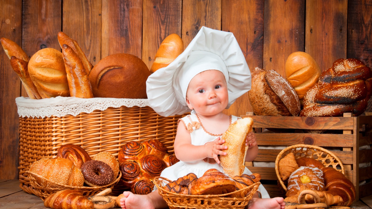 Маленький мальчик в костюме повара сидит на столе с выпечкой