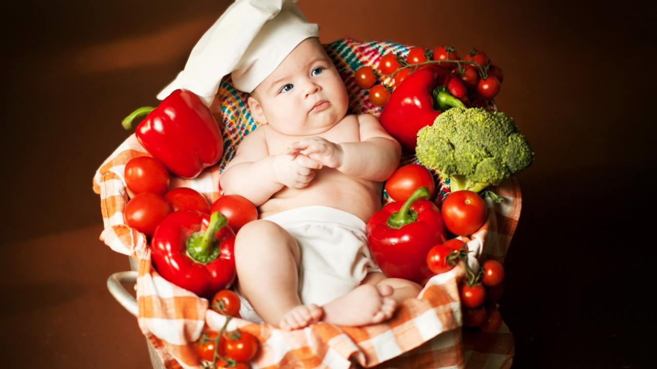 Маленький мальчик в костюме повара в корзине с перцем и помидорами