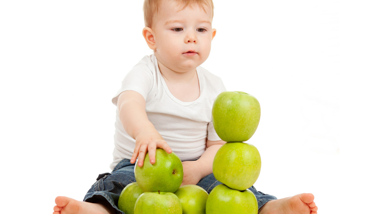 Маленький мальчик играет с зелеными яблоками на белом фоне