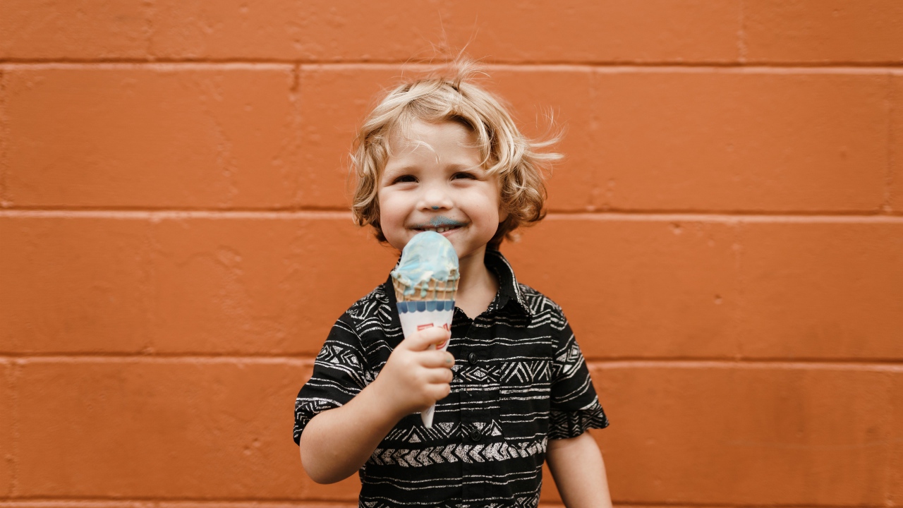 Маленький мальчик с мороженым в руках у стены